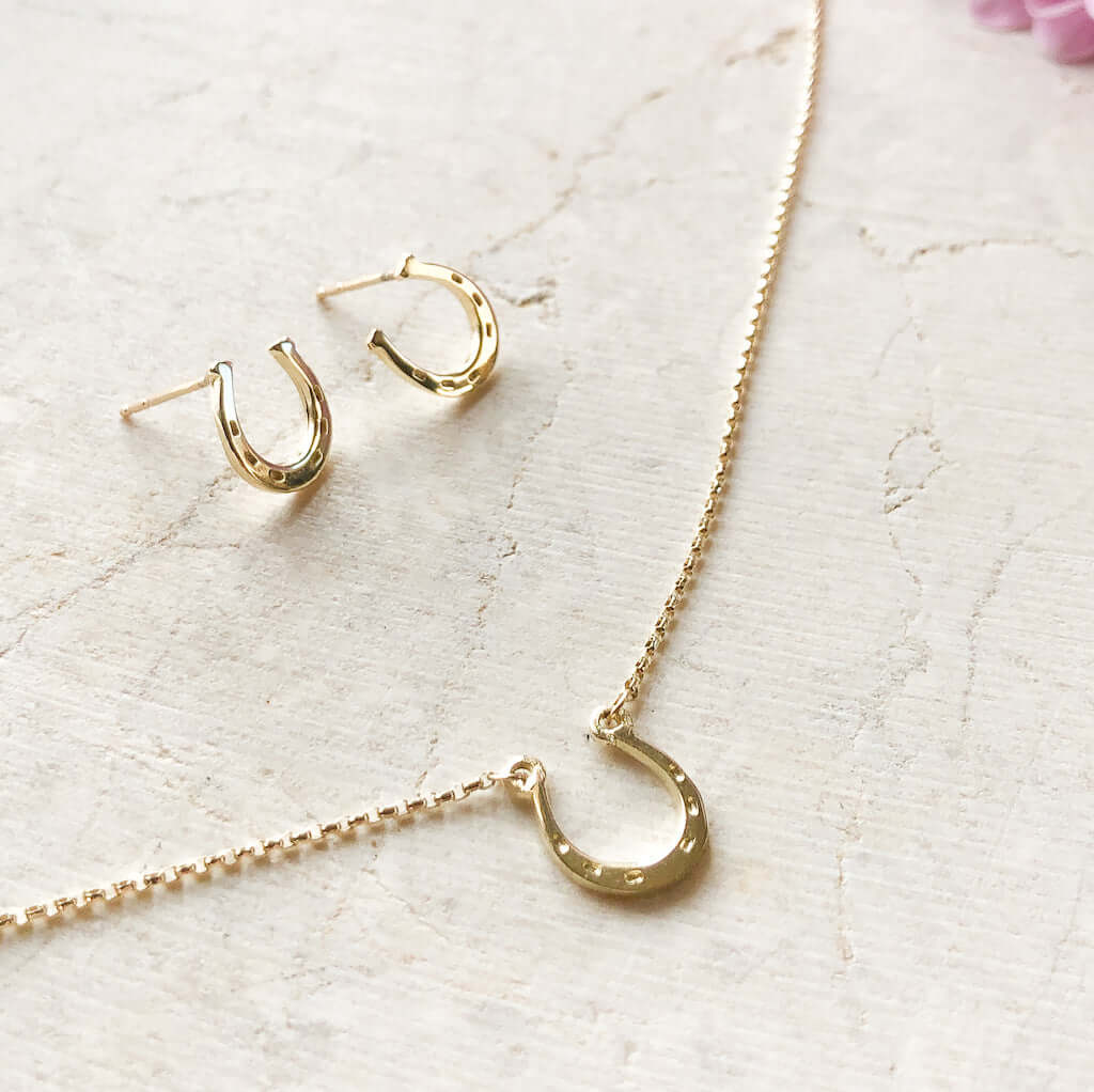 9ct gold horseshoe stud earrings with a matching horseshoe necklace laid out on a cream stone 