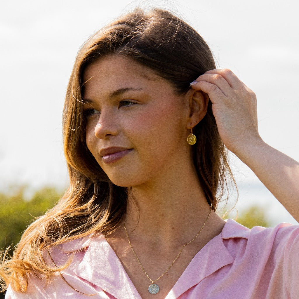 a woman outside wearing dara knot drop earrings with a matching necklace tucking her hair behind her ear